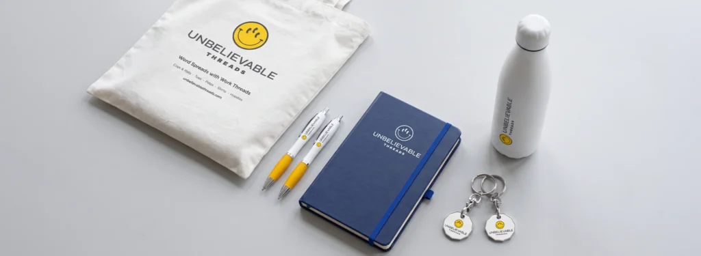 Branded promotional giveaways including logo bugs, pens, notebooks, tote bags, reusable bottles and keyrings.